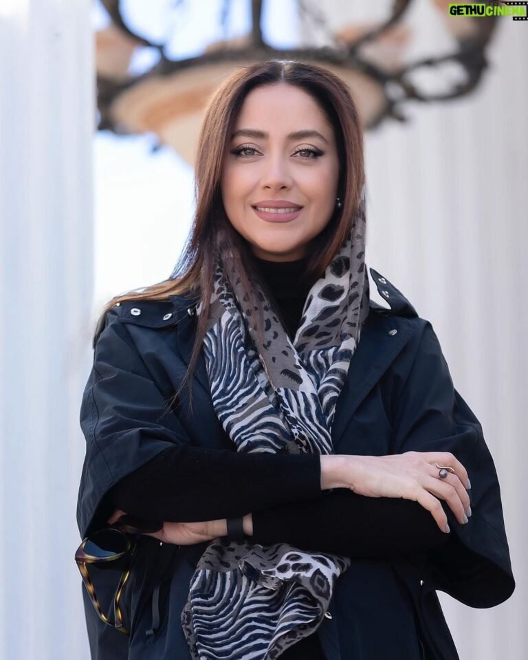 persian model with long dark hair wearing a white lace dress looking into camera