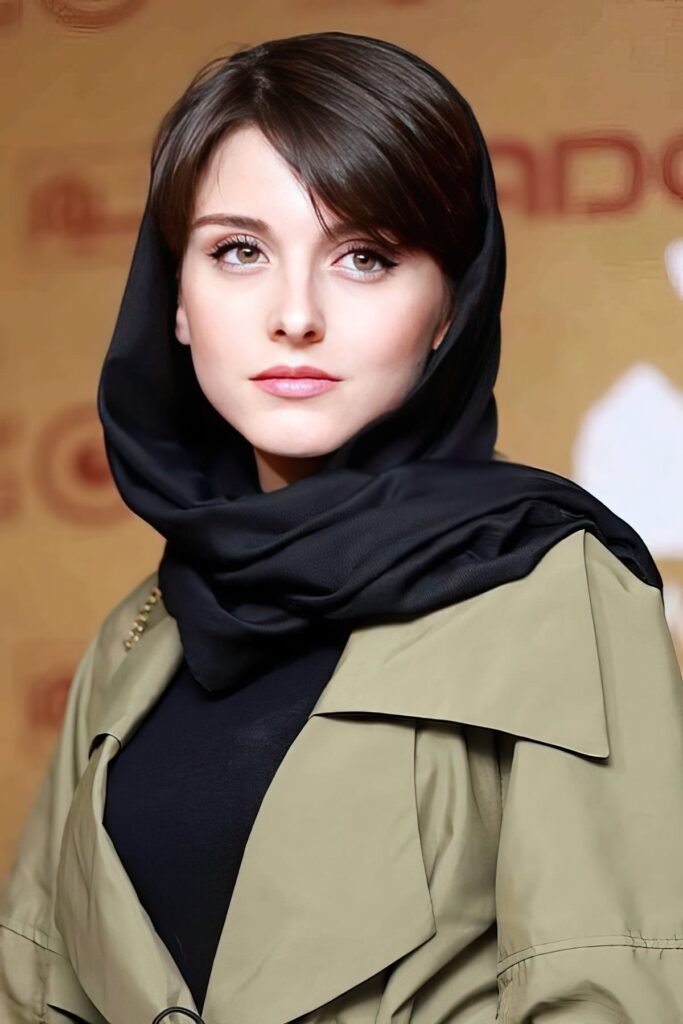 persian actress with long dark hair wearing a dark navy blue coat with silver accessories looking into camera