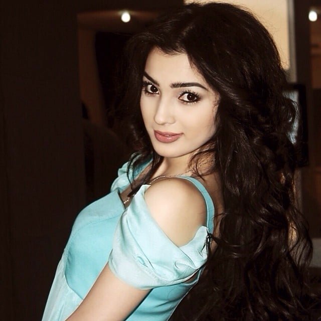 persian model with long dark hair looking into camera wearing a white top