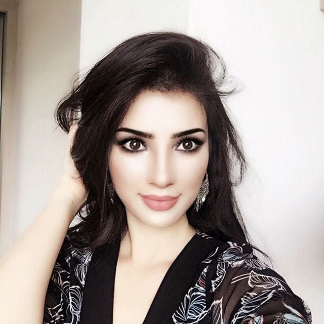 persian model with long dark hair smiling while wearing a white tank top